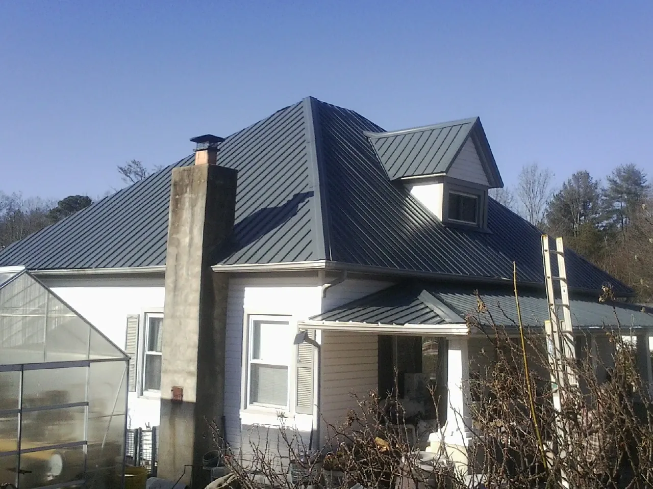 Dark blue standing seam metal roof on a white farmhouse with dormer — Slate & Tile Roof Repair by Roofing Brothers in Mumford