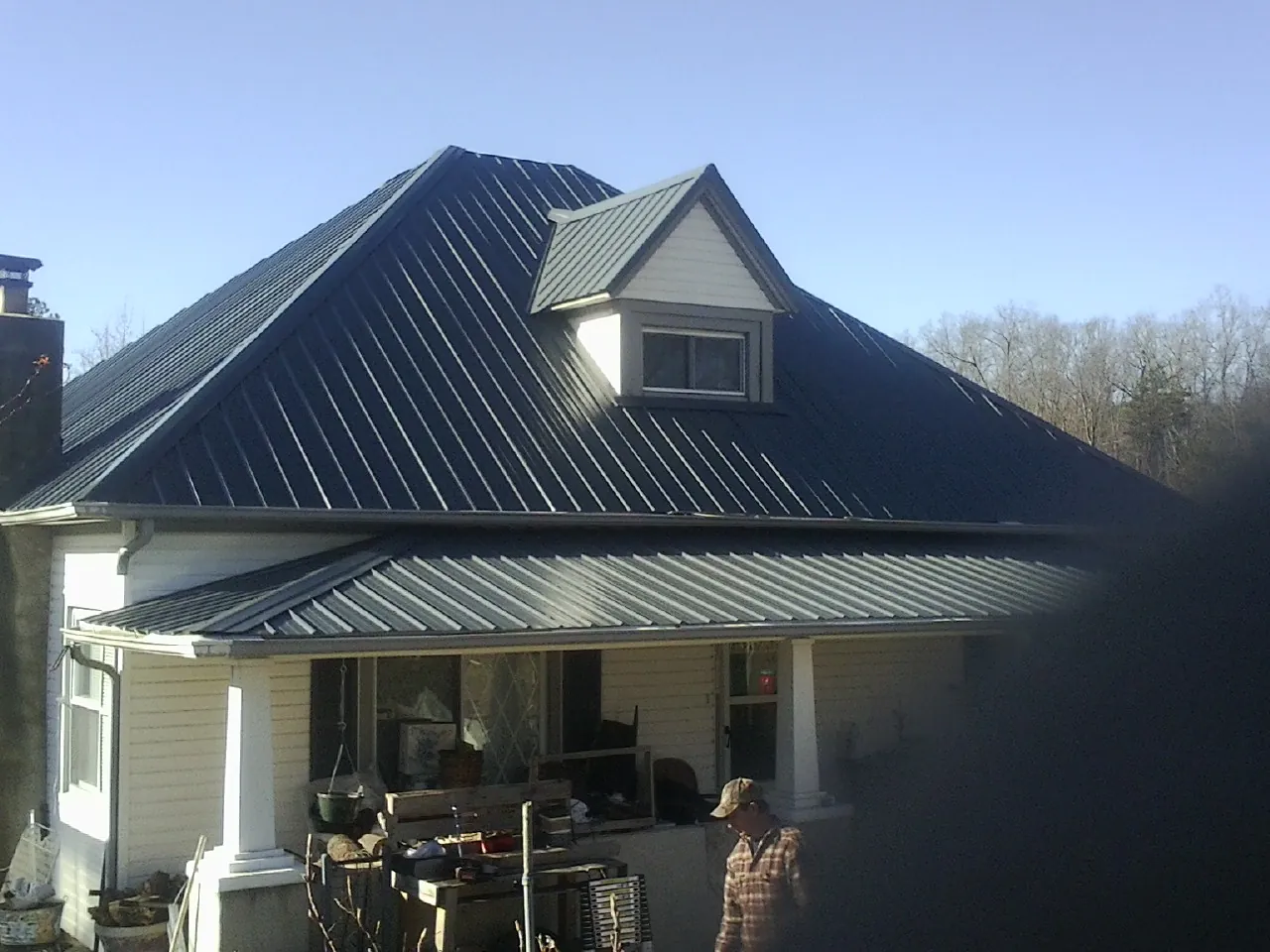 Dark blue standing seam metal roof with a dormer above a front porch in Mumford