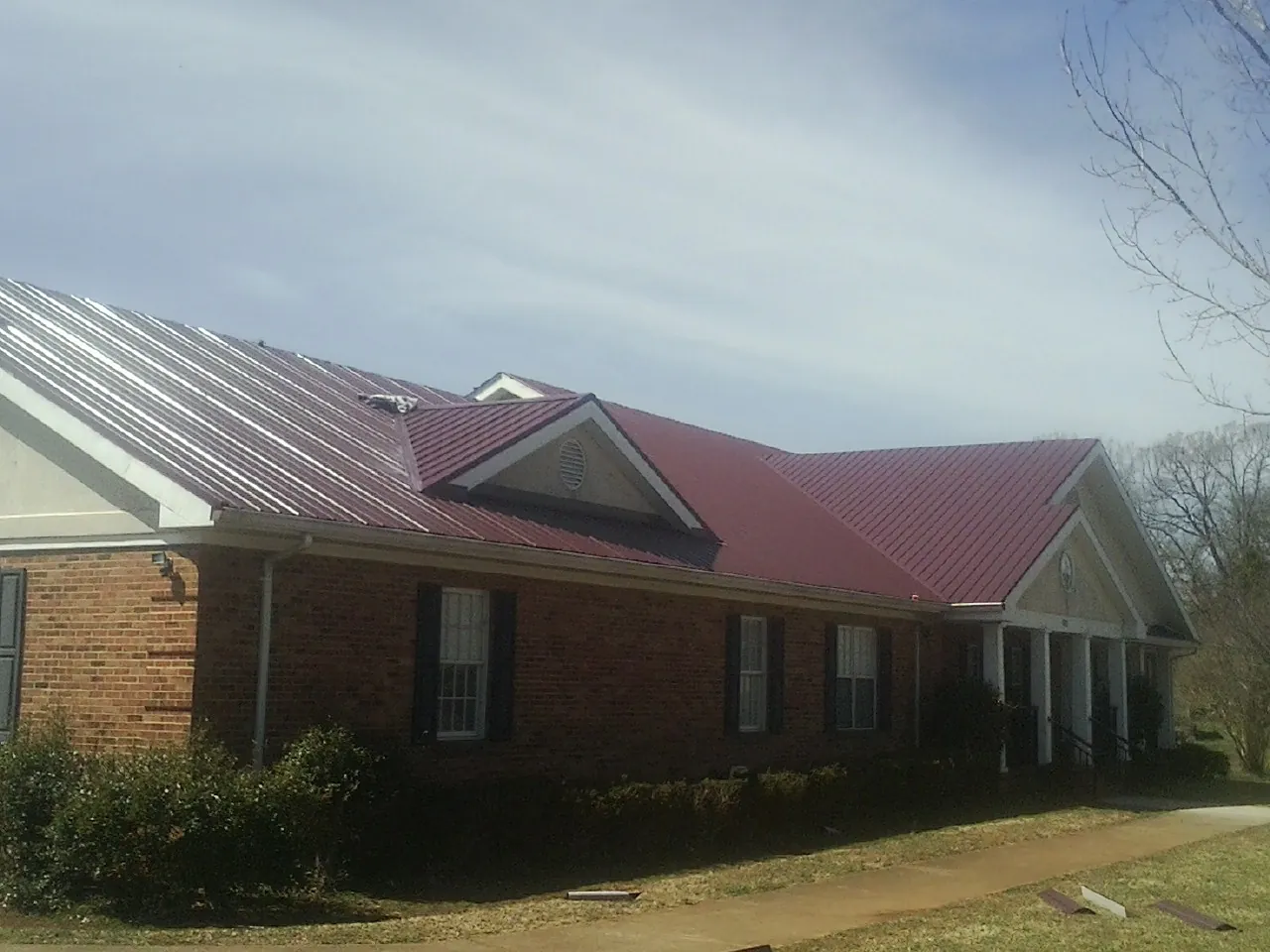 Red metal roof with gabled entries on a long brick building, from a Hail Damage Roof Repair job in Mumford