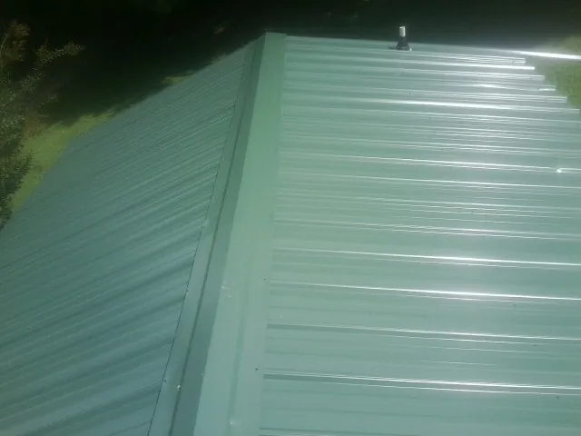 New green metal panels meeting at the ridge of a roof — Flat Roof Repair work by our crew in Mumford