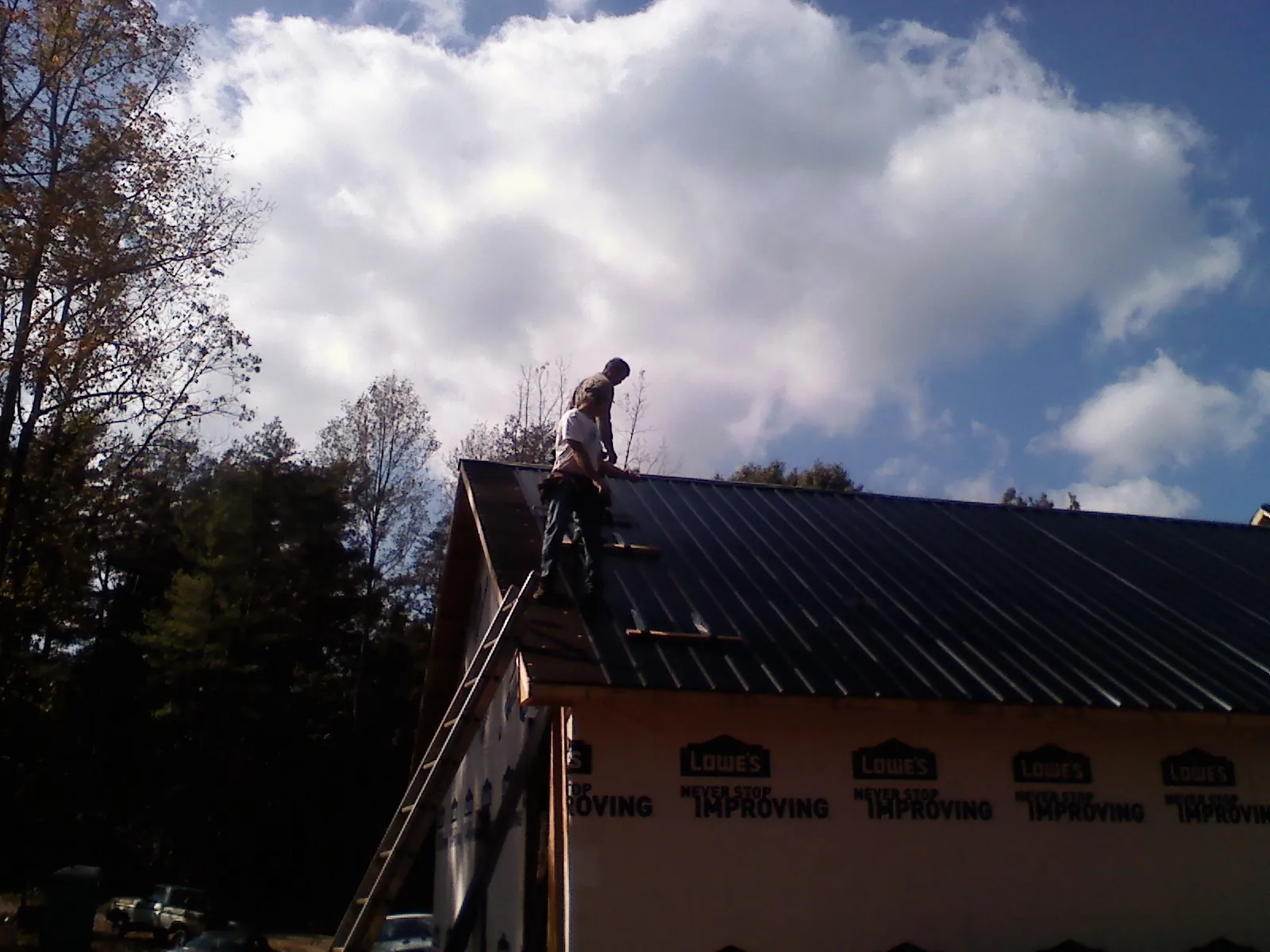Roofer fastening dark metal panels high against a cloudy sky, from a Roof Inspection job in Mumford