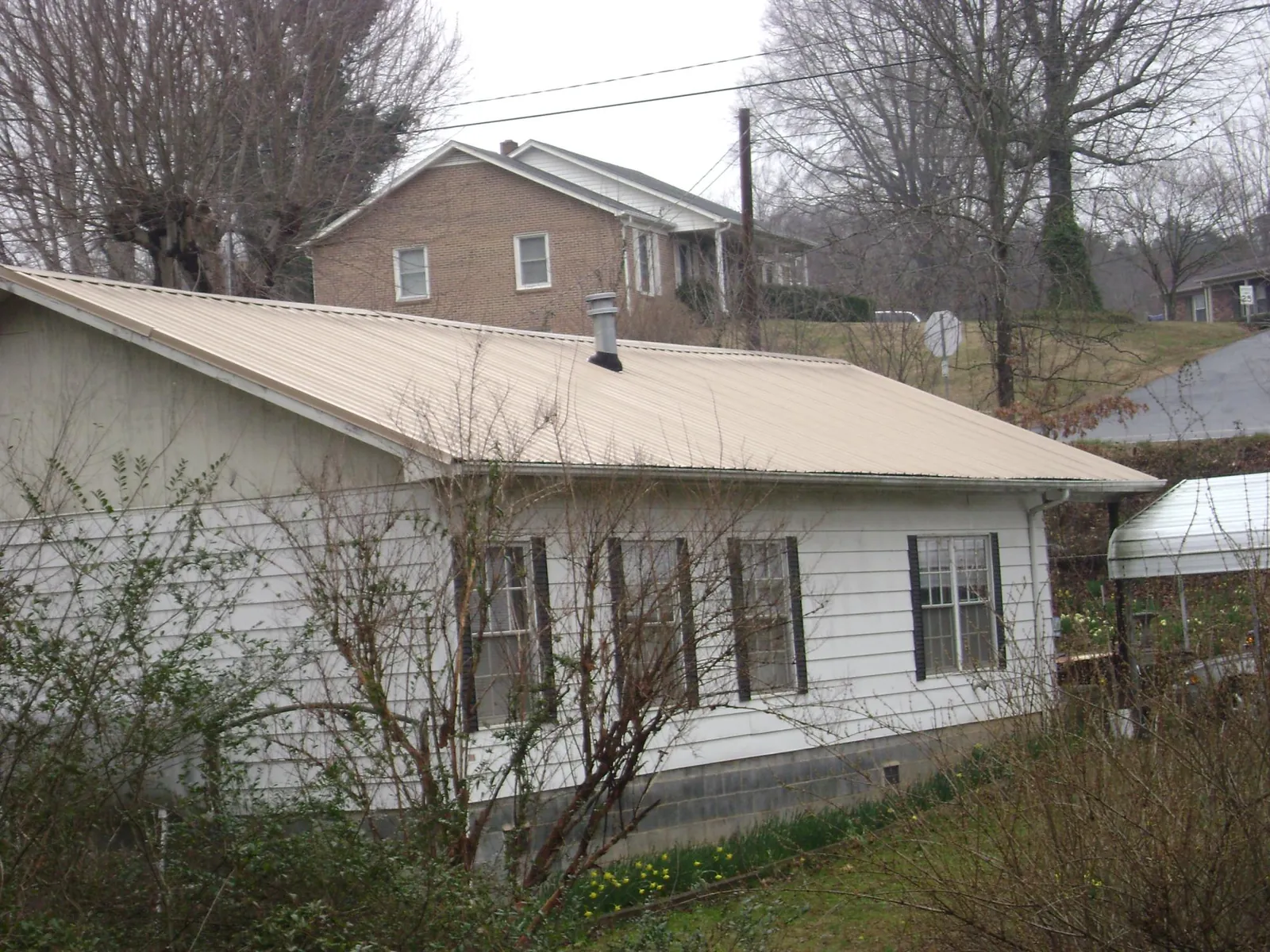 Tan metal roof on a white sided house set into a hillside — Commercial Roofing by Roofing Brothers in Mumford