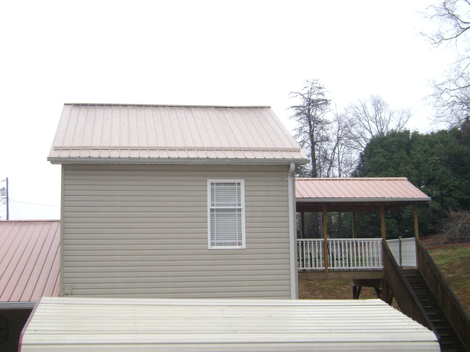 Tan metal roofs on a two story addition and attached porch, from a Roof Replacement job in Mumford